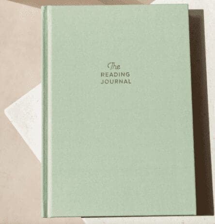 A minimalist reading journal with a light green hardcover. The cover features the title 'The Reading Journal' written in small, elegant font in the center. The journal is placed on a light-colored surface, creating a simple and serene aesthetic. The design is clean and understated, making it an ideal gift for book lovers who enjoy keeping track of their reading experiences.